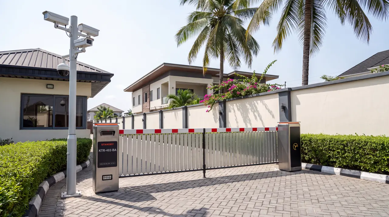 A SecureGate vehicle lane in daylight: a stainless barrier cabinet and a reader column beside a fenced boom across the driveway, with a camera mast carrying three bullet cameras and a dome above them.